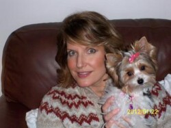 A woman sitting on a brown leather couch holding a small dog with a pink bow. Date on image: 2012/01/22.
